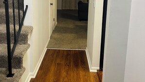 A staircase with a black handrail leading to a carpeted landing. A door opens to a room with a curtain and a chair. - Spacious2 - bedroom condo in tranquil (Reynoldsburg)