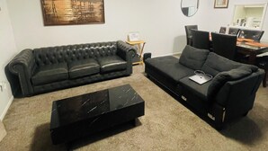A living room with a black leather sofa, a black ottoman, and a coffee table. There is a painting on the wall, a round mirror, and a ceiling fan. - Spacious2 - bedroom condo in tranquil (Reynoldsburg)