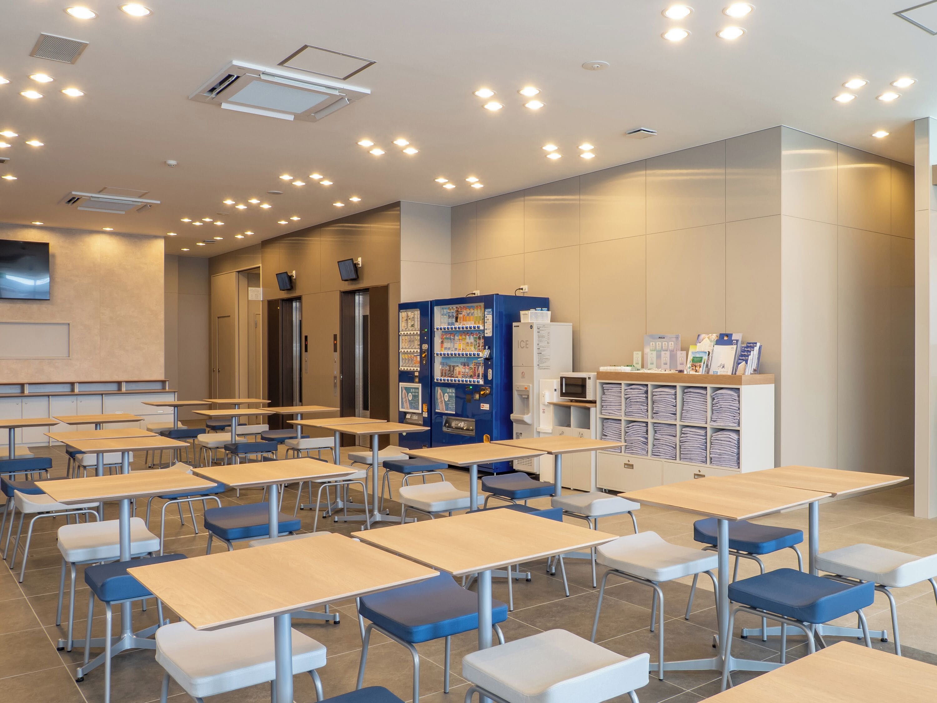 A classroom with desks, chairs, a vending machine, and a refrigerator.