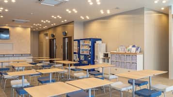 A classroom with desks, chairs, a vending machine, and a refrigerator.