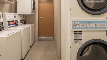 A laundry facility with multiple washing machines and dryers, a door with a sign, and a tiled floor.