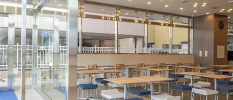 A modern dining area with tables and chairs, a glass partition, and a clock on the wall.