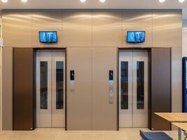 Un par de puertas de ascensor con pantallas digitales, una pequeña mesa y un banco.