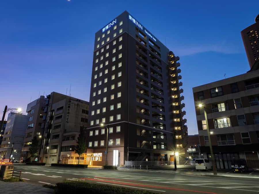 A multi-story hotel with a prominent sign at the top, a well-lit entrance, and a parking area in the foreground.