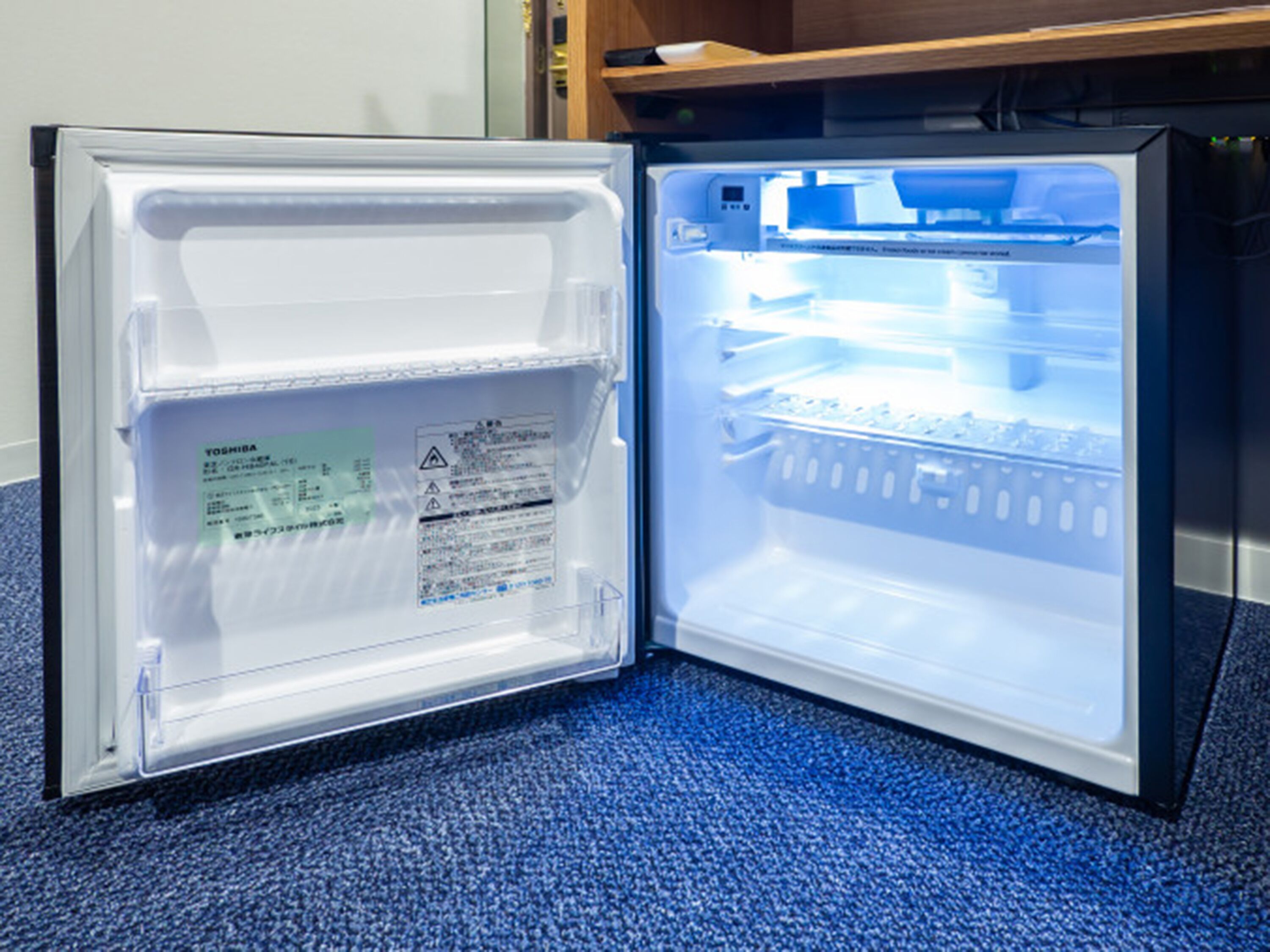 An open refrigerator with a blue interior, a visible water bottle, and a label on the door.