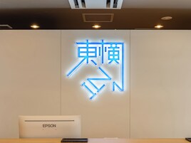 Ein Empfangsschalter mit einer Neonreklame in einer Fremdsprache, einem Wandlüfter und einem Schild mit der Aufschrift 'EPSON'.