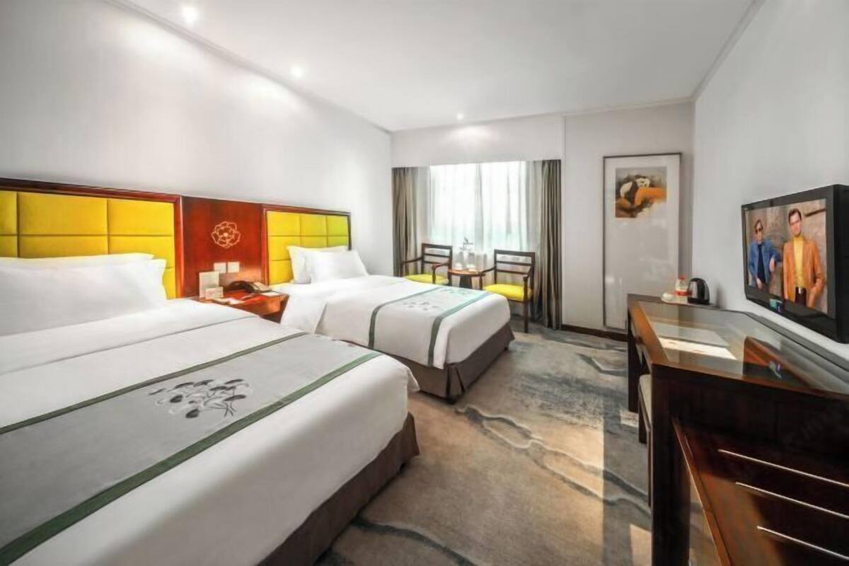 A hotel room with two beds, a desk, a chair, and a television.