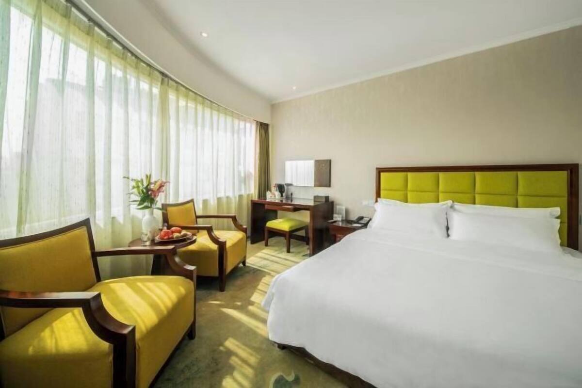 A hotel room with a bed, a desk, a chair, and a window with curtains.