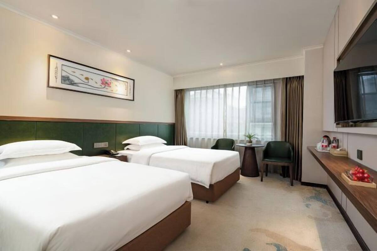 A hotel room with two beds, a desk, a chair, a television, and a window with curtains.