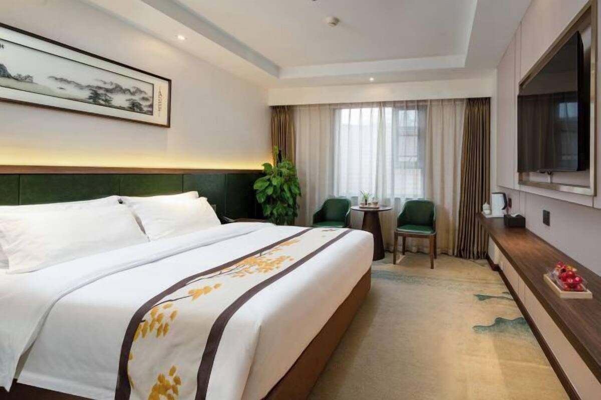 A hotel room with a bed, a television, a desk with a chair, and a window with curtains.