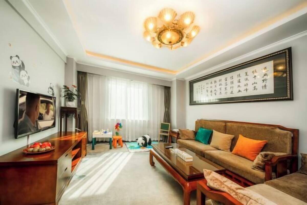 A living room with a sofa, coffee table, TV, and a framed calligraphy piece on the wall.