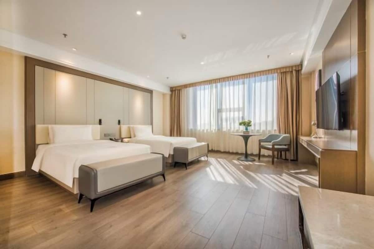 Een hotelkamer met twee bedden, een bureau, een stoel, een televisie en een raam met gordijnen.