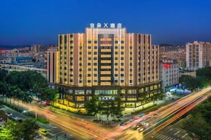 A multi-story hotel with a modern facade, surrounded by a busy street with light trails indicating traffic.
