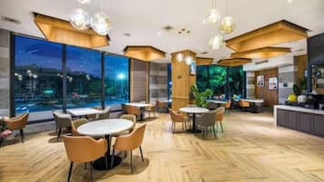 A modern restaurant with round tables and chairs, large windows, and a view of the city at night.