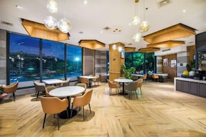 A modern restaurant with round tables and chairs, large windows, and a view of the city at night.