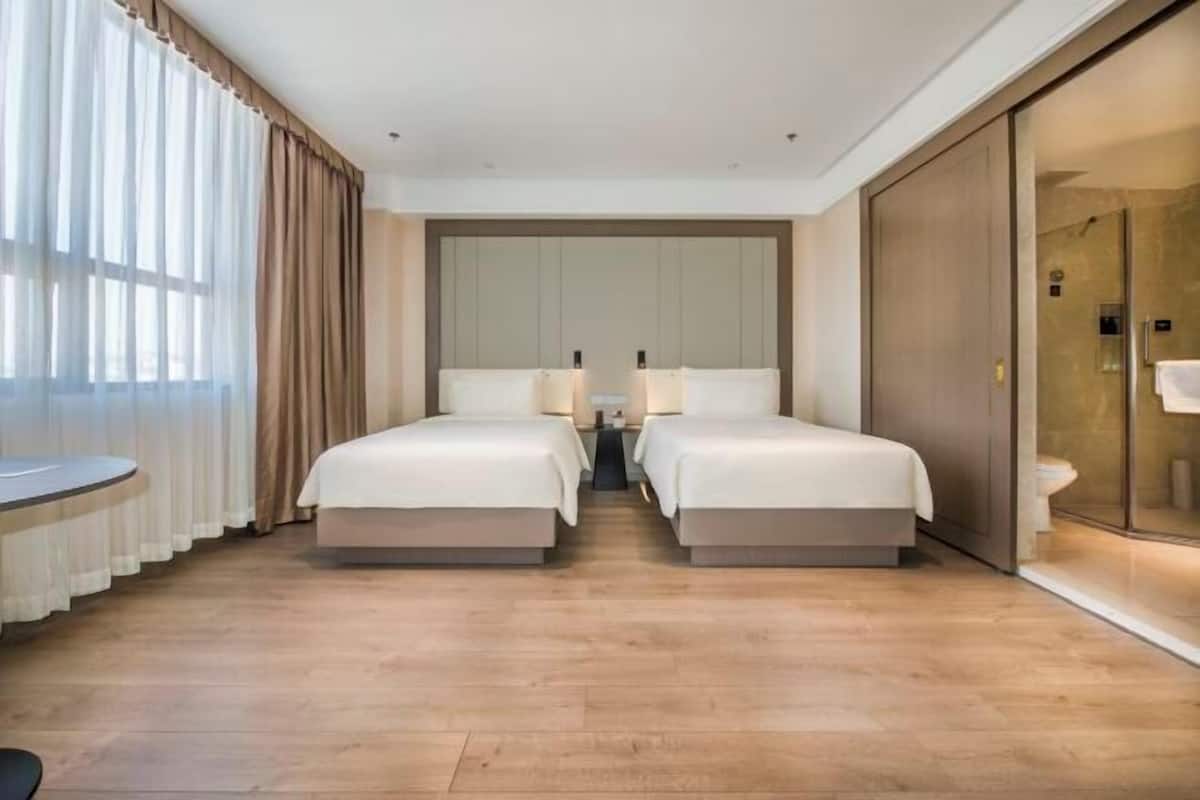 Een hotelkamer met twee bedden, een grote spiegel, een nachtkastje, een douchecabine van glas en uitzicht op het omliggende landschap.