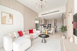 Ein modernes Wohnzimmer mit einem weißen Sofa, einem runden Couchtisch und einem durch eine offene Tür einsehbarer Küchenbereich.