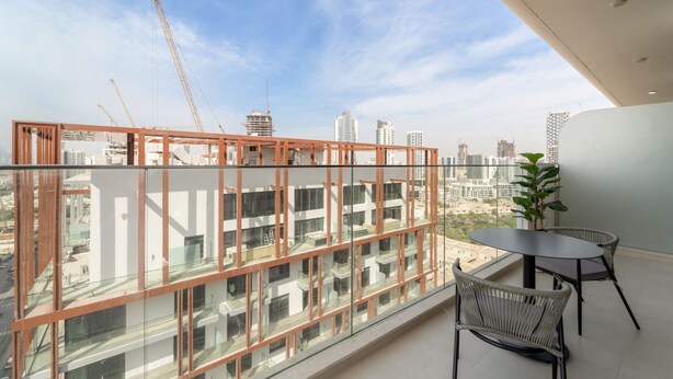 A balcony with a glass railing, a potted plant, and a table with chairs. - Pearl House II - 1104 1BD (Dubai)