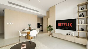 A modern living room with a large flat-screen TV, a dining area with white chairs, and a minimalist design. - Pearl House II - 1104 1BD (Dubai)