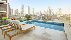 A rooftop pool with lounge chairs, a clear view of a city skyline, and modern buildings in the background. - Pearl House II - 1104 1BD (Dubai)