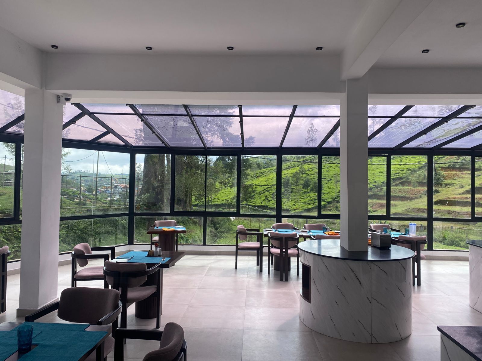 A modern dining area with large windows and a view of a green landscape.