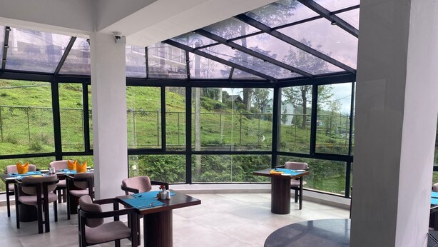 A modern dining area with large windows, a round table, and several chairs. - Hotel Montagna  (Nuwara Eliya)