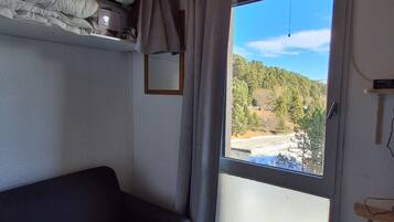 Una habitación con un sofá de color oscuro, techo de madera, ventana con vistas a un área boscosa y una puerta con marco de madera.