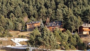 Un bâtiment coiffé d’un toit en tuiles, entouré de plaques de neige et adossé à une colline boisée.