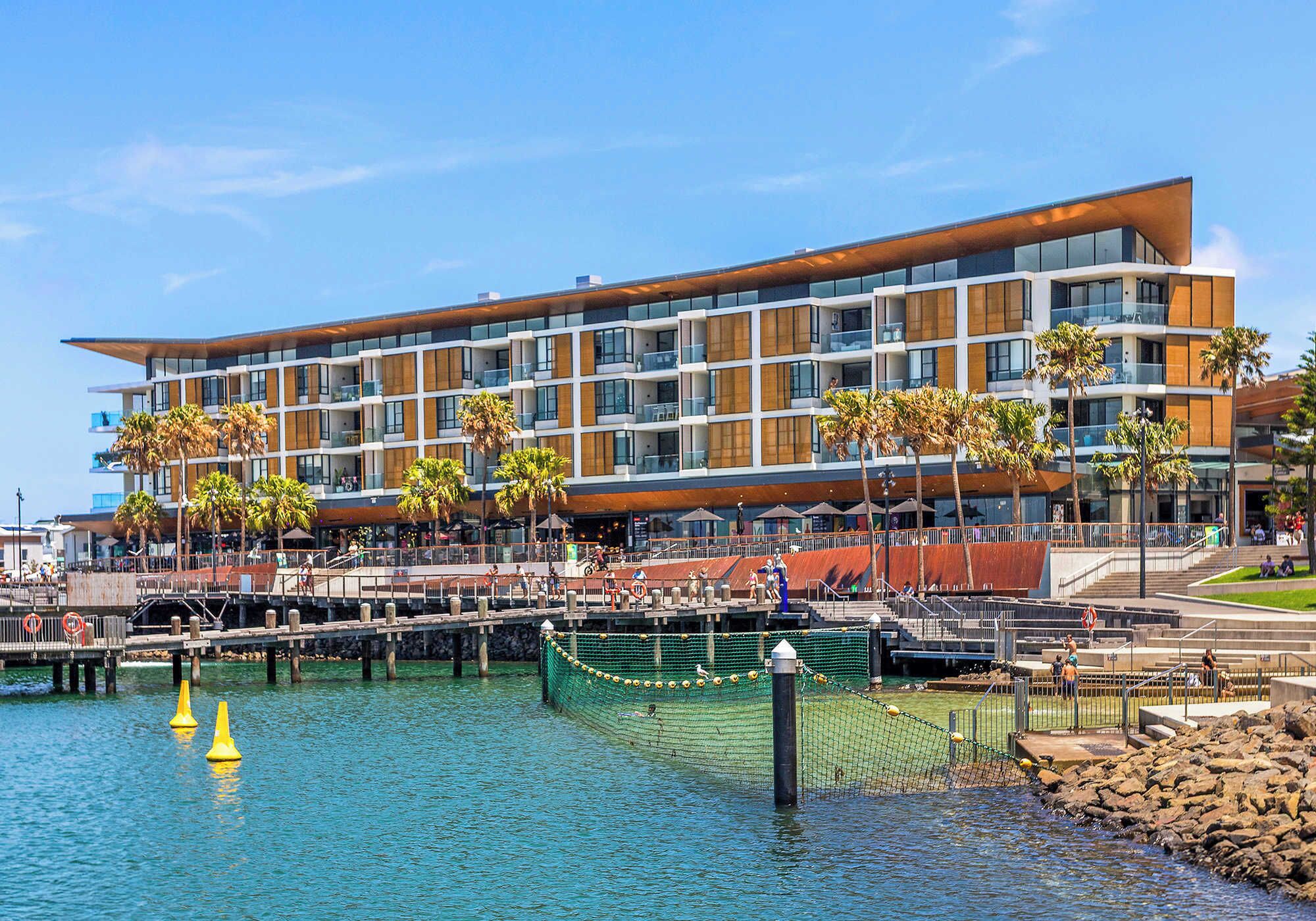 A modern hotel with multiple floors, a waterfront view, and a dock area with yellow buoys.