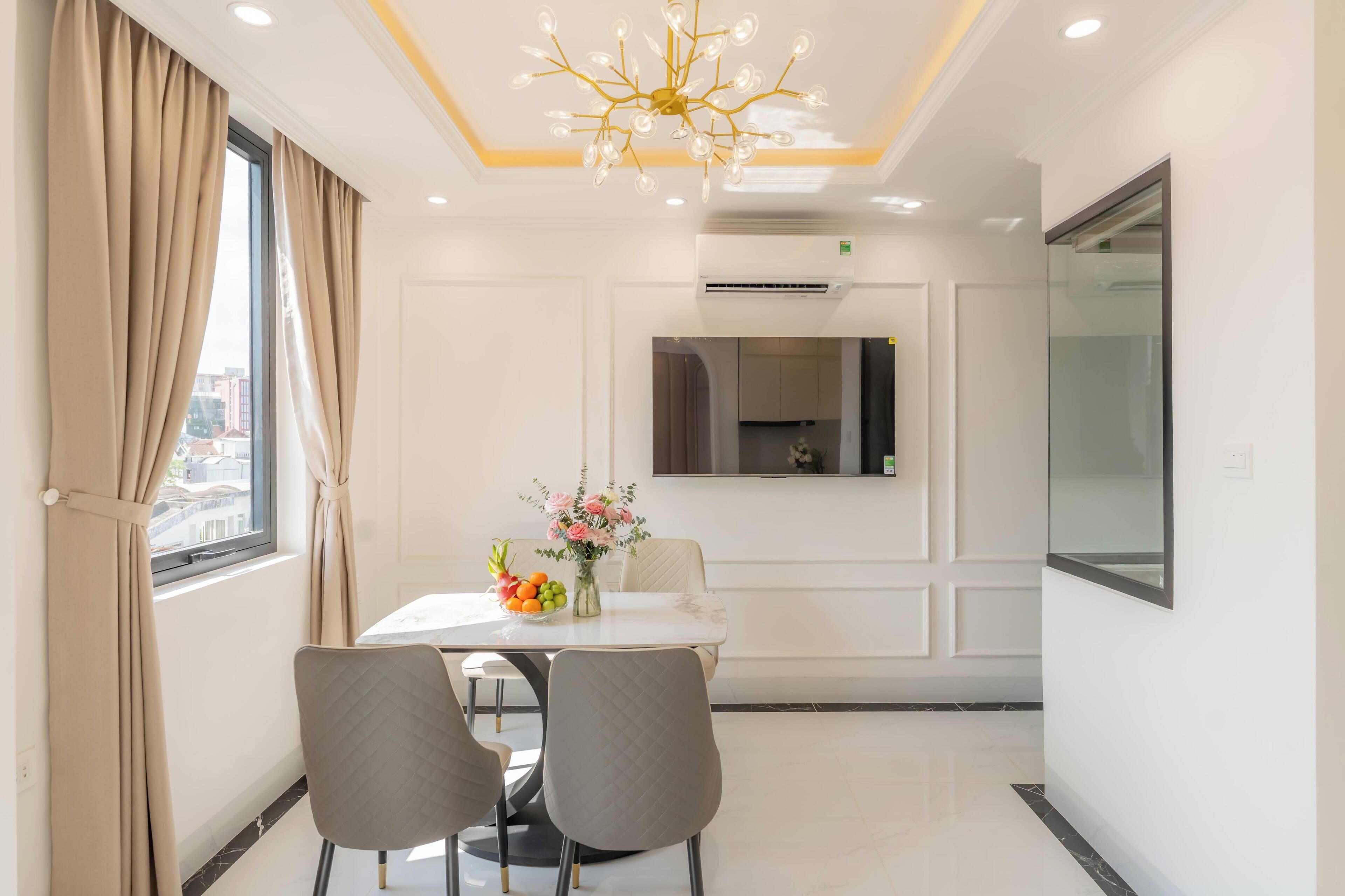 A modern dining area with a white table, two chairs, a chandelier, and a vase of flowers.
