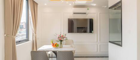 A modern dining area with a white table, two chairs, a chandelier, and a vase of flowers.