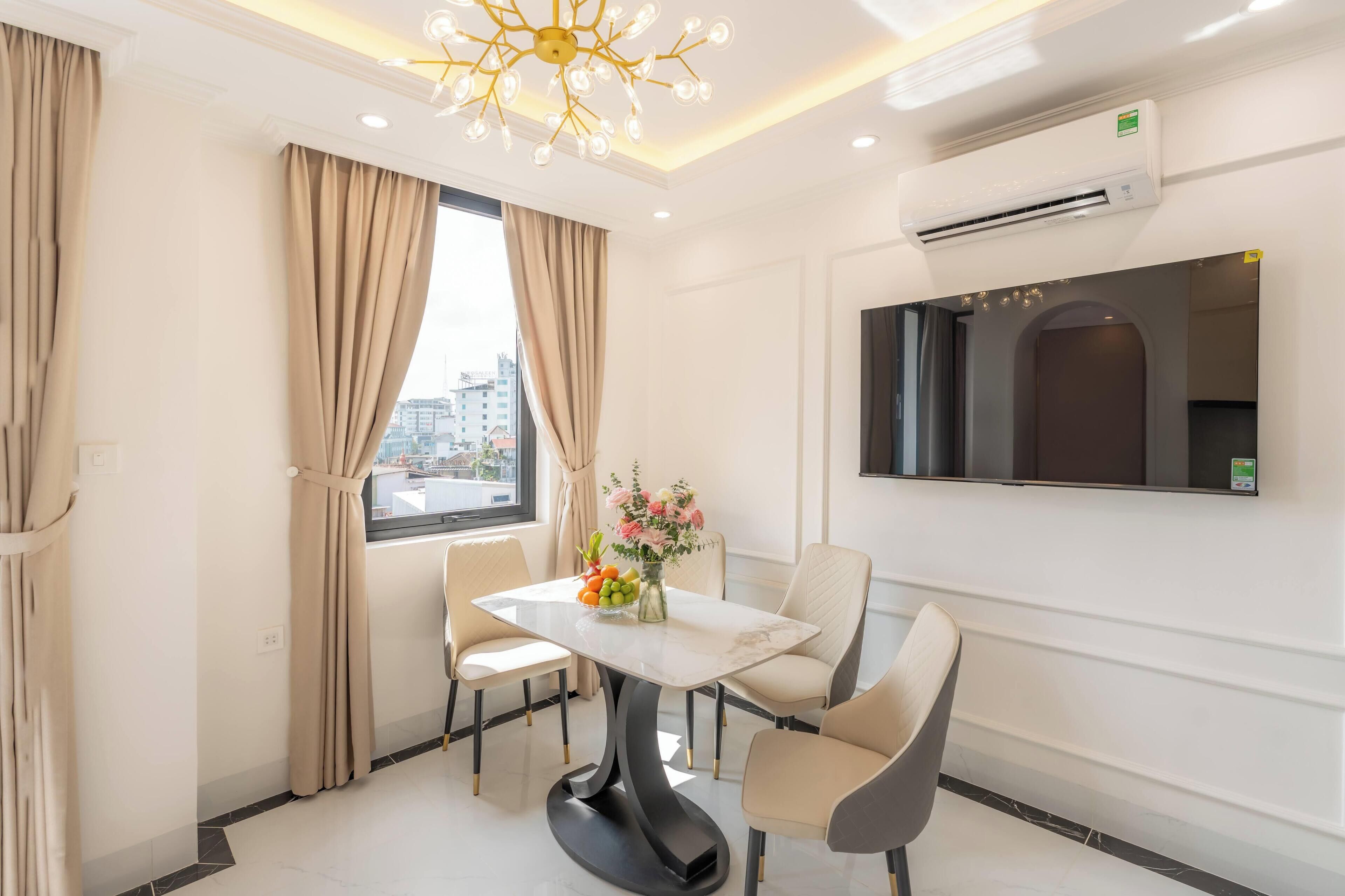 A modern hotel room with a dining area featuring a marble table, beige chairs, and a vase of flowers.