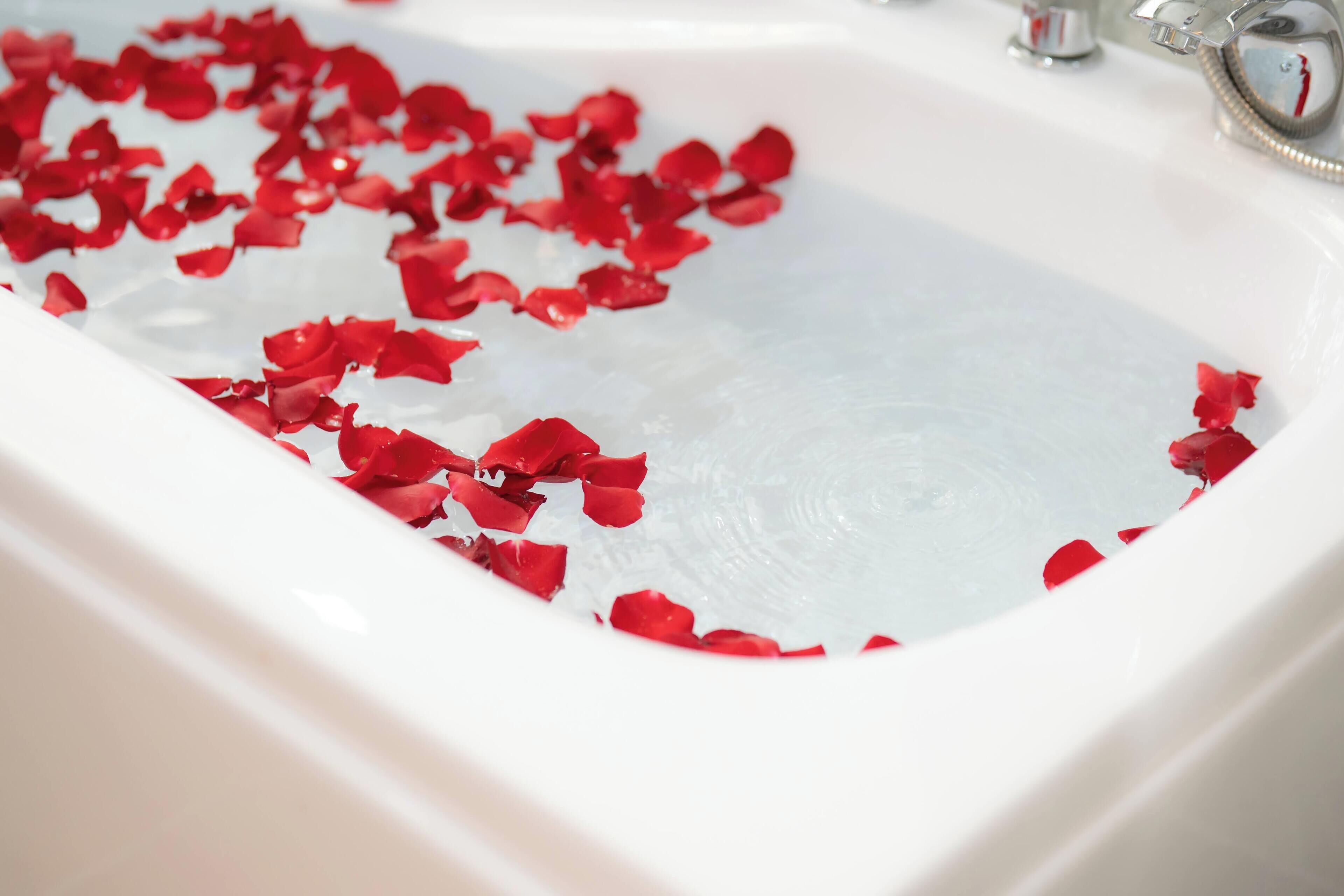 A white sink with red rose petals scattered in the water.