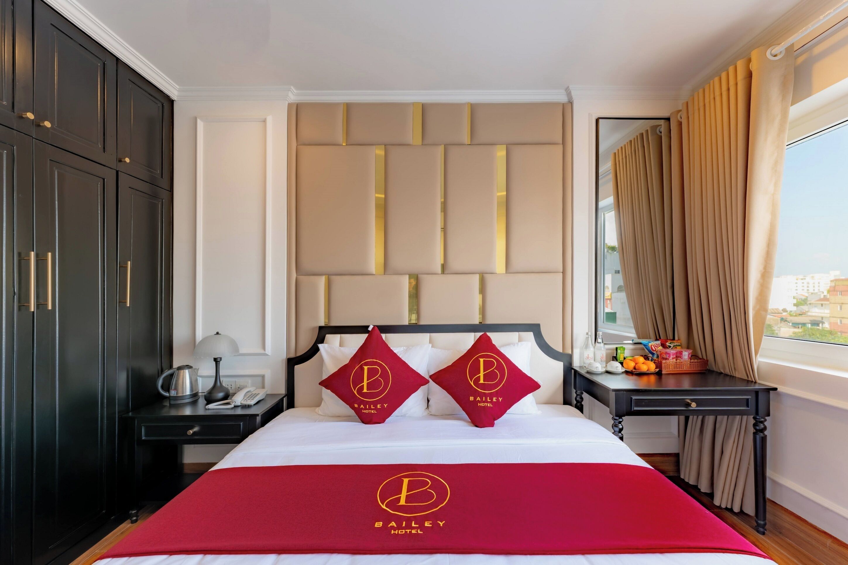 A hotel room with a bed, a nightstand, a lamp, a phone, a tray table, and a window with curtains.