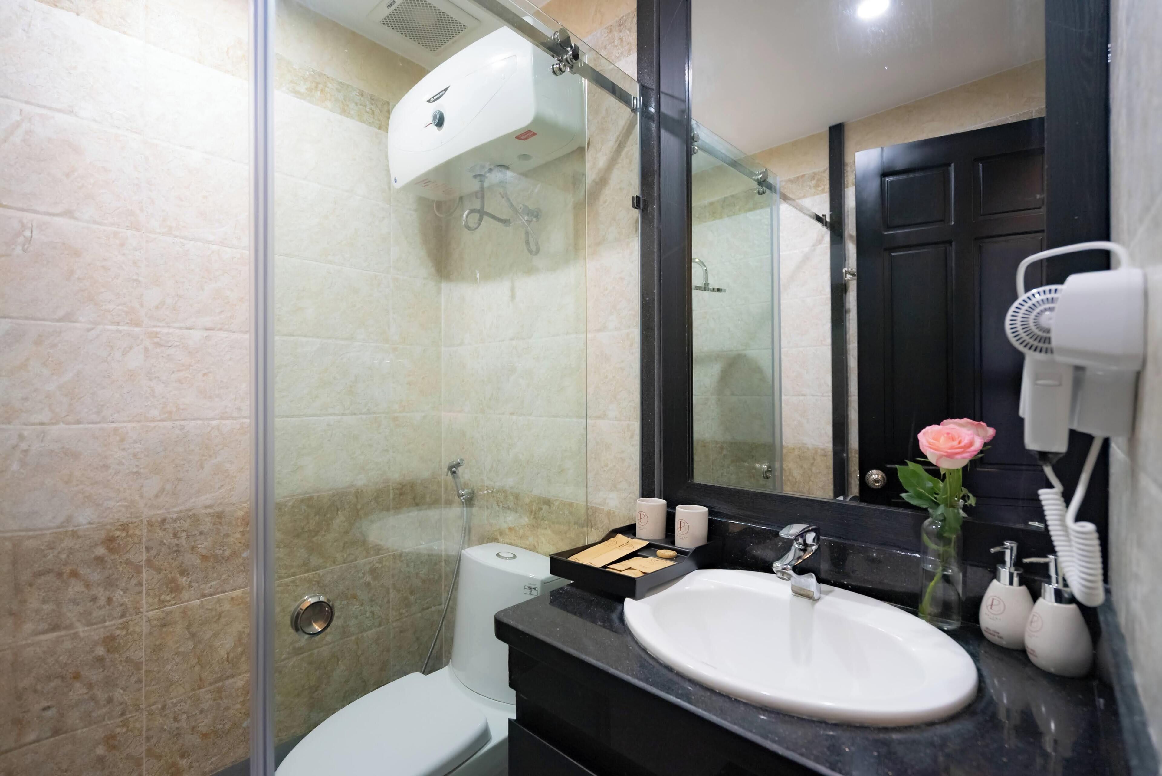 A modern bathroom with a glass shower enclosure, a white toilet, a black sink with a mirror above it, and a vase with a pink rose.