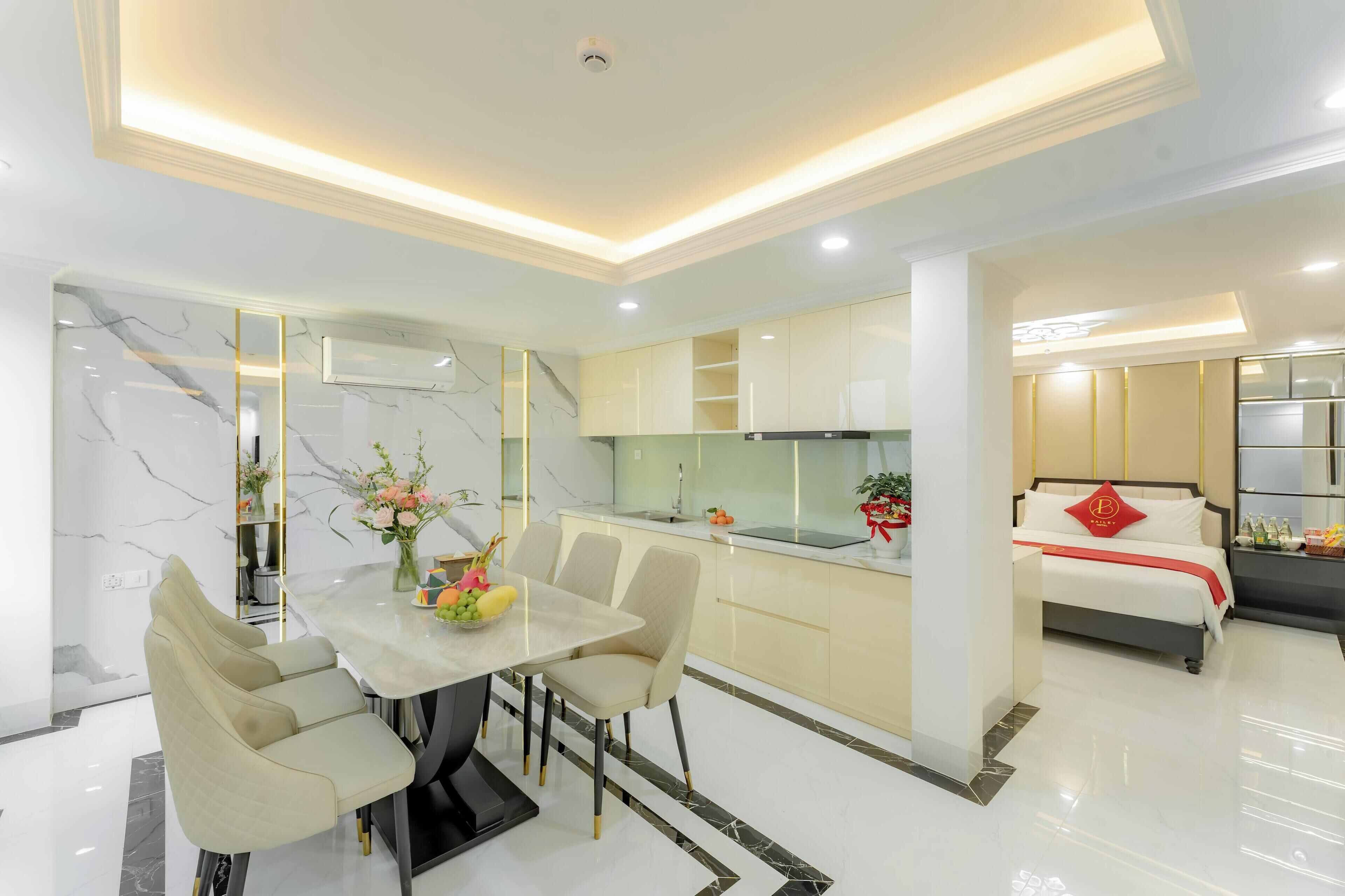 A modern hotel room with a dining area, a kitchen, and a bed.