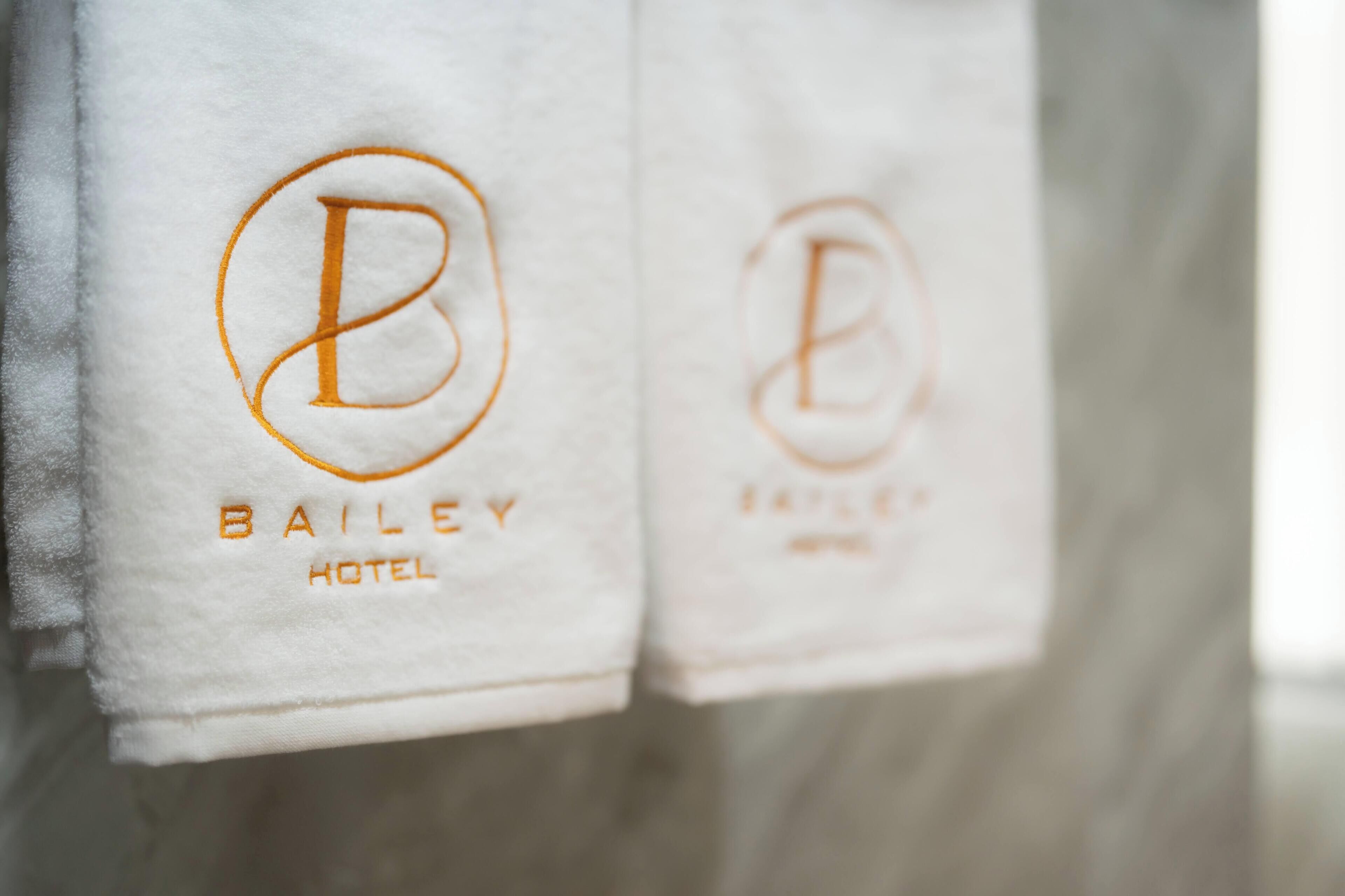 Two towels hanging on a wall with embroidered logos and the text "BAILEY HOTEL".