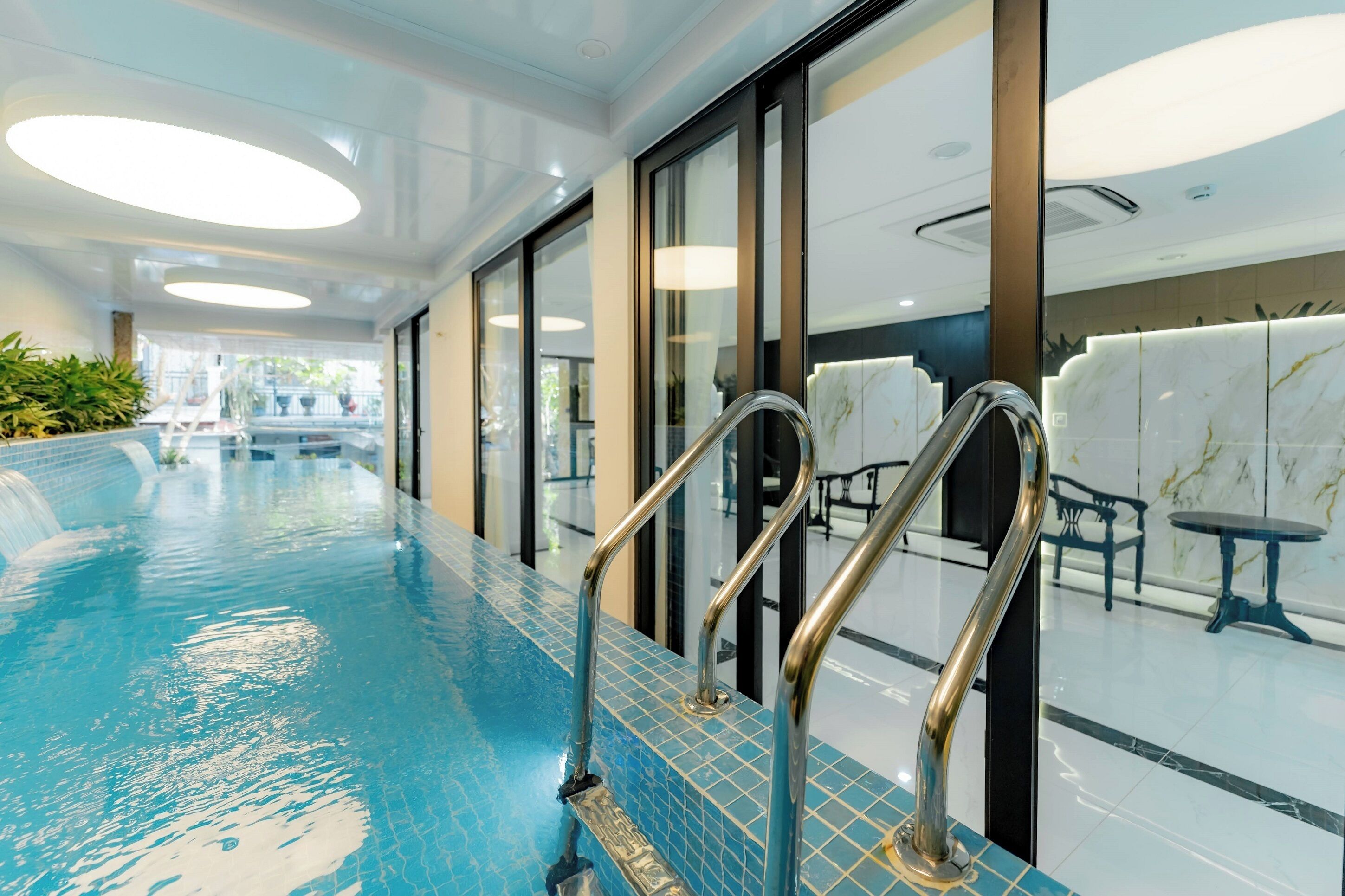 An indoor swimming pool with clear blue water, metal handrails, and a tiled floor.
