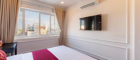 Quarto de hotel com uma cama grande, televisão na parede e janela com cortinas.
