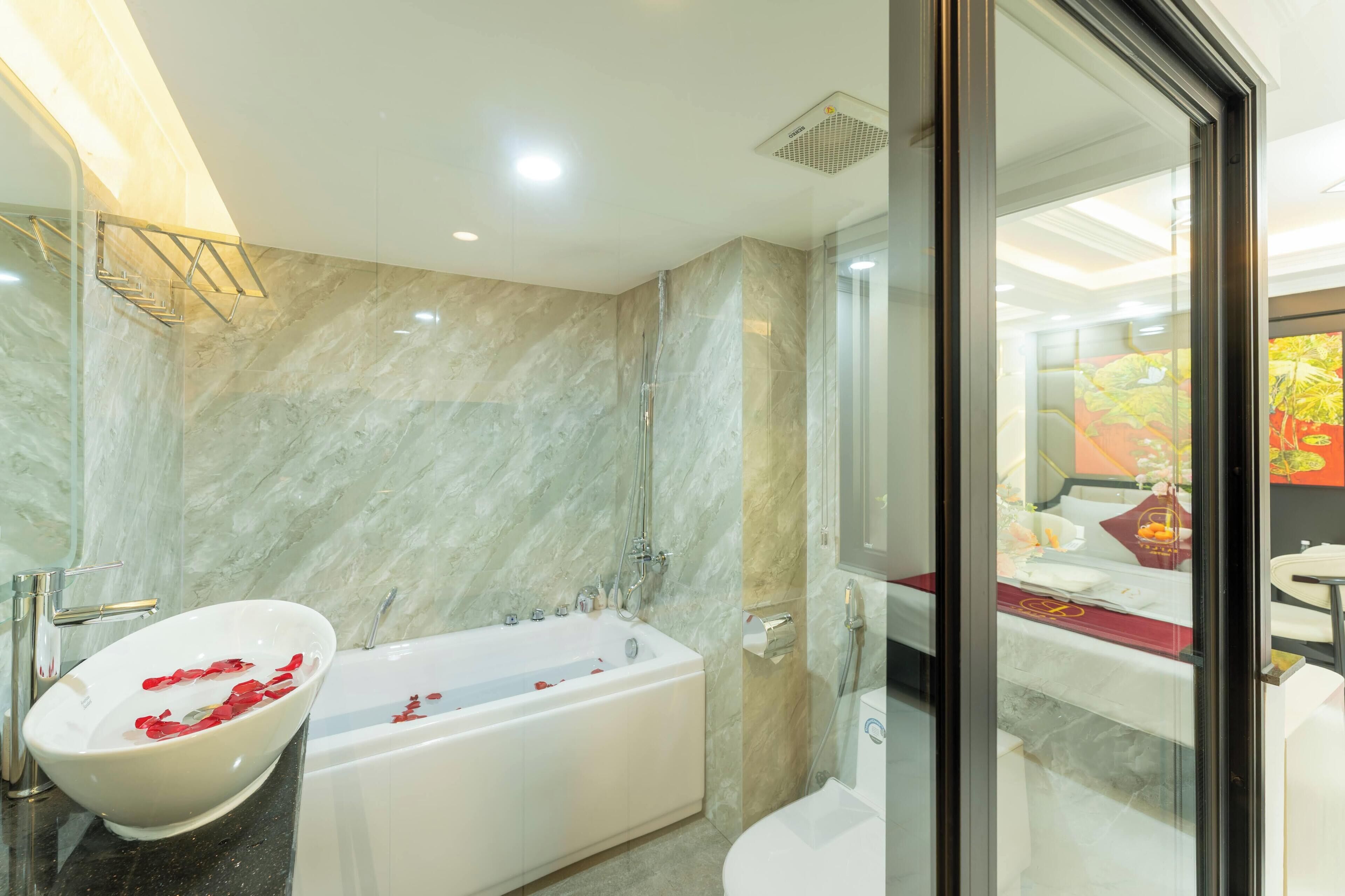 Un baño moderno con pared de mármol, una bañera independiente y zona de ducha con mampara de vidrio.