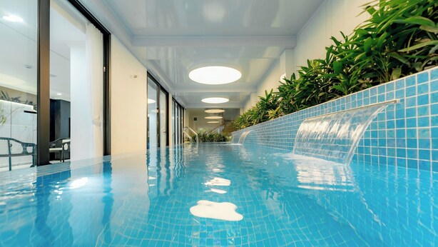 A swimming pool with a clear blue tile floor, a water feature on the right, and a staircase leading to an upper level. - Bailey Hotel Hue (Hue)