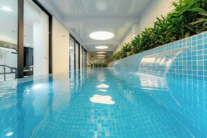 A swimming pool with a clear blue tile floor, a water feature on the right, and a staircase leading to an upper level. - Bailey Hotel Hue (Hue)