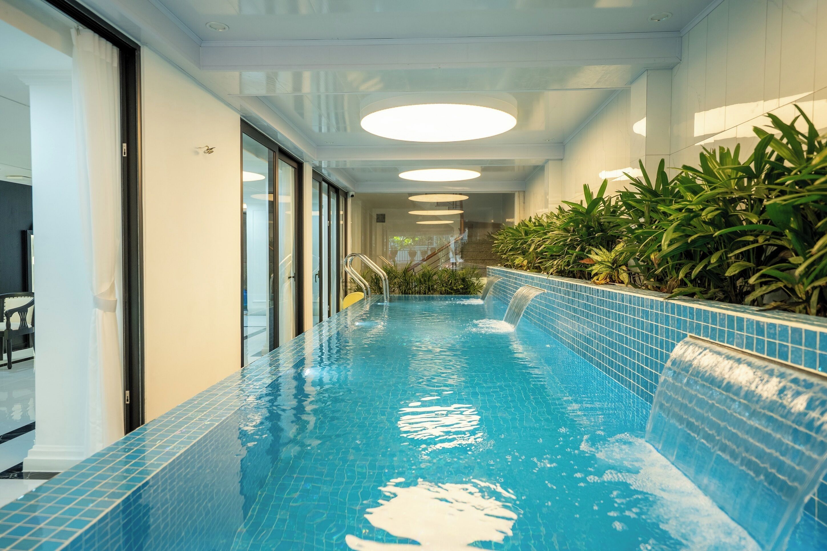 An indoor swimming pool with a tiled edge, a glass door entrance, and a staircase leading to a higher level.