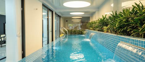 An indoor swimming pool with a tiled edge, a glass door entrance, and a staircase leading to a higher level.