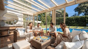Una habitació il·luminada pel sol amb sostre de vidre, mobles de vimet i una piscina al fons.
