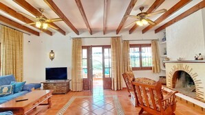 Uma sala de estar com televisão, sofá, cadeiras de madeira, lareira e ventoinha no teto.