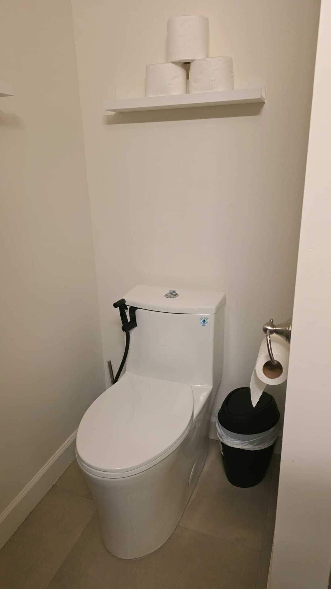 Des toilettes avec un réservoir, un porte-rouleau et une poubelle noire.