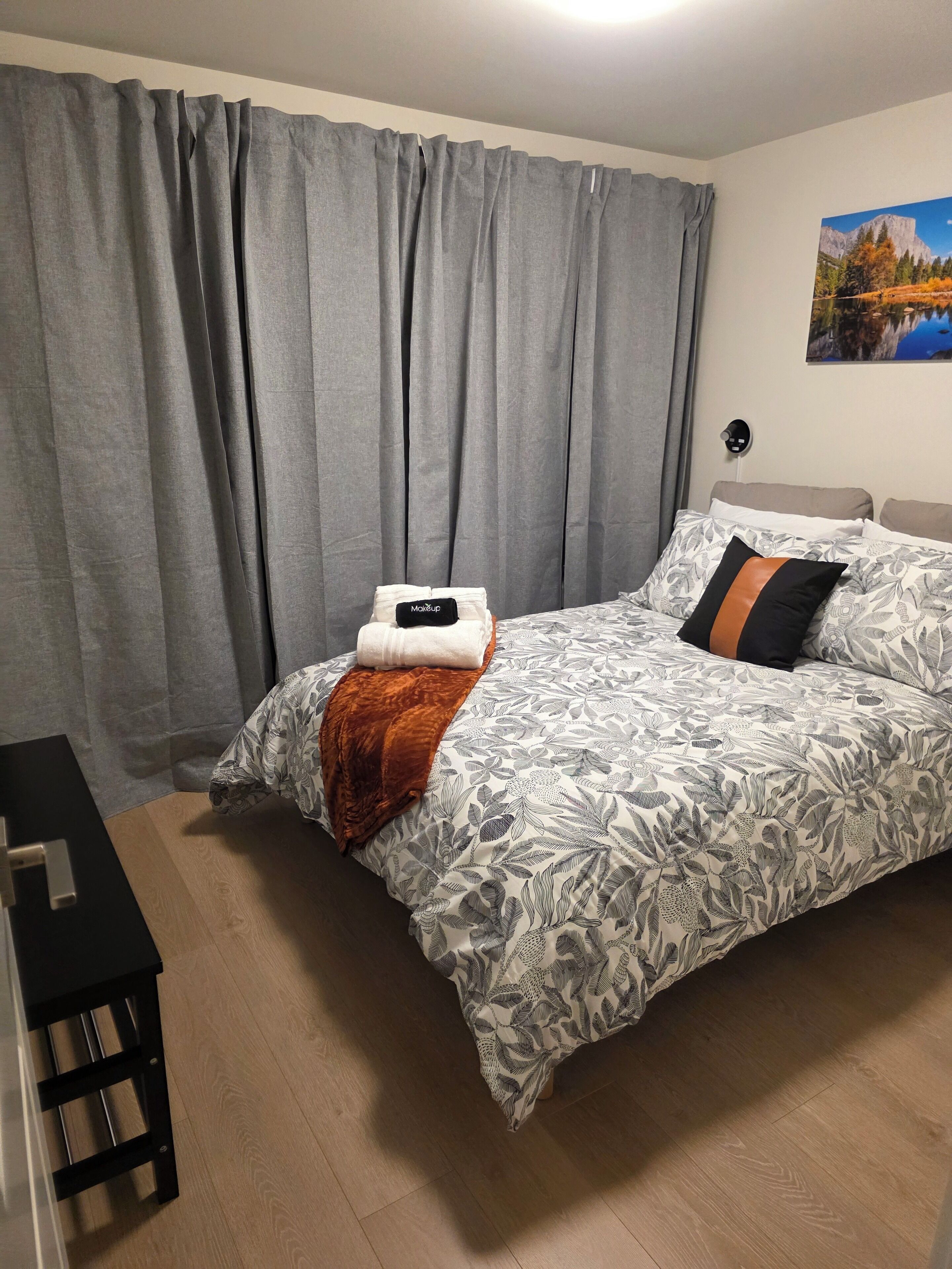 Ein Schlafzimmer mit einem Bett, grauen Vorhängen, einem Gemälde und einem Nachttisch.
