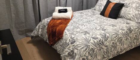 Ein Schlafzimmer mit einem Bett, grauen Vorhängen, einem Gemälde und einem Nachttisch.