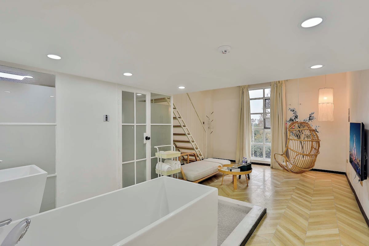 Un salon moderne avec une baignoire blanche, un escalier, un fauteuil suspendu et un téléviseur fixé au mur.